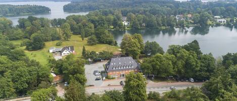 An aerial view of a lakeside property with a large house, a parking area, and surrounding greenery.