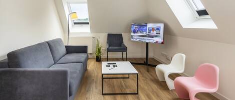 A modern living room with a grey sofa, a white coffee table, a TV, and two chairs.