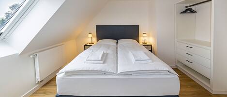 A modern bedroom with a skylight, a bed with white linens, bedside lamps, and a wardrobe.