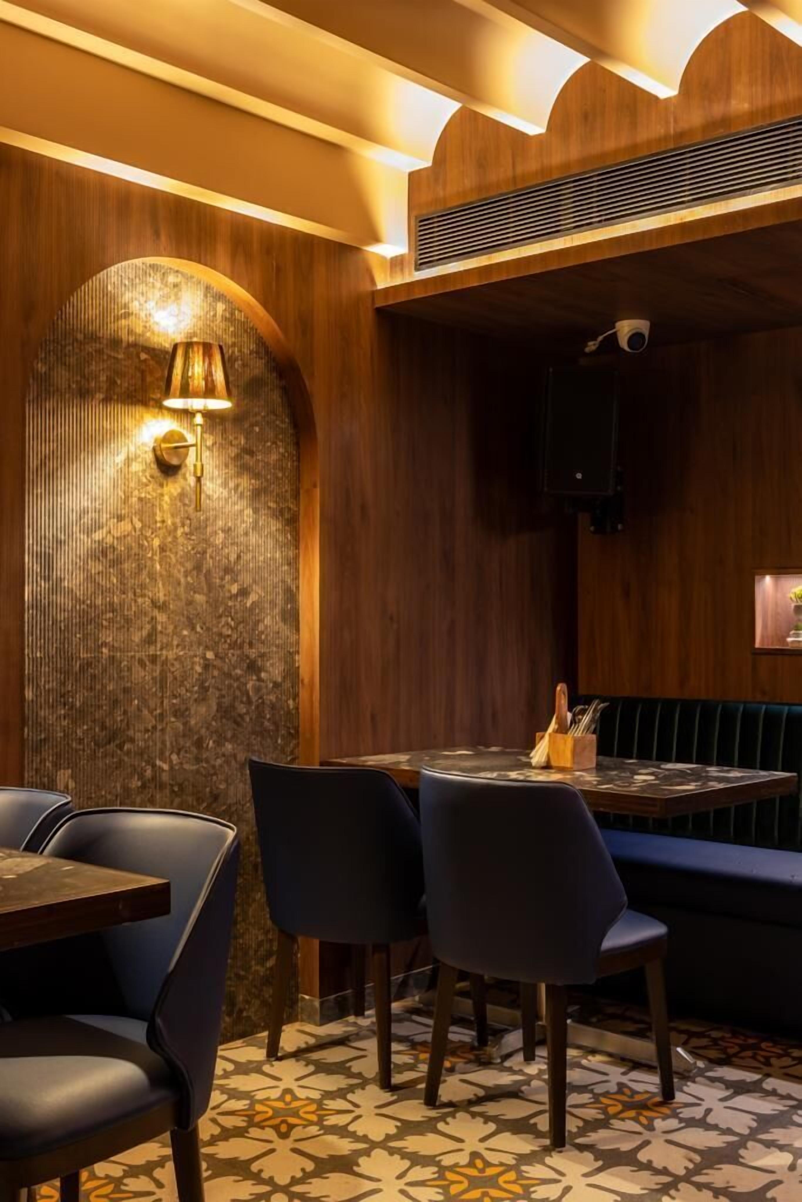 Interior de restaurante con paneles de madera, suelo estampado y zona de estar con mesas y sillas.