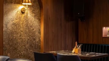 Interior de restaurante con paneles de madera, suelo estampado y zona de estar con mesas y sillas.