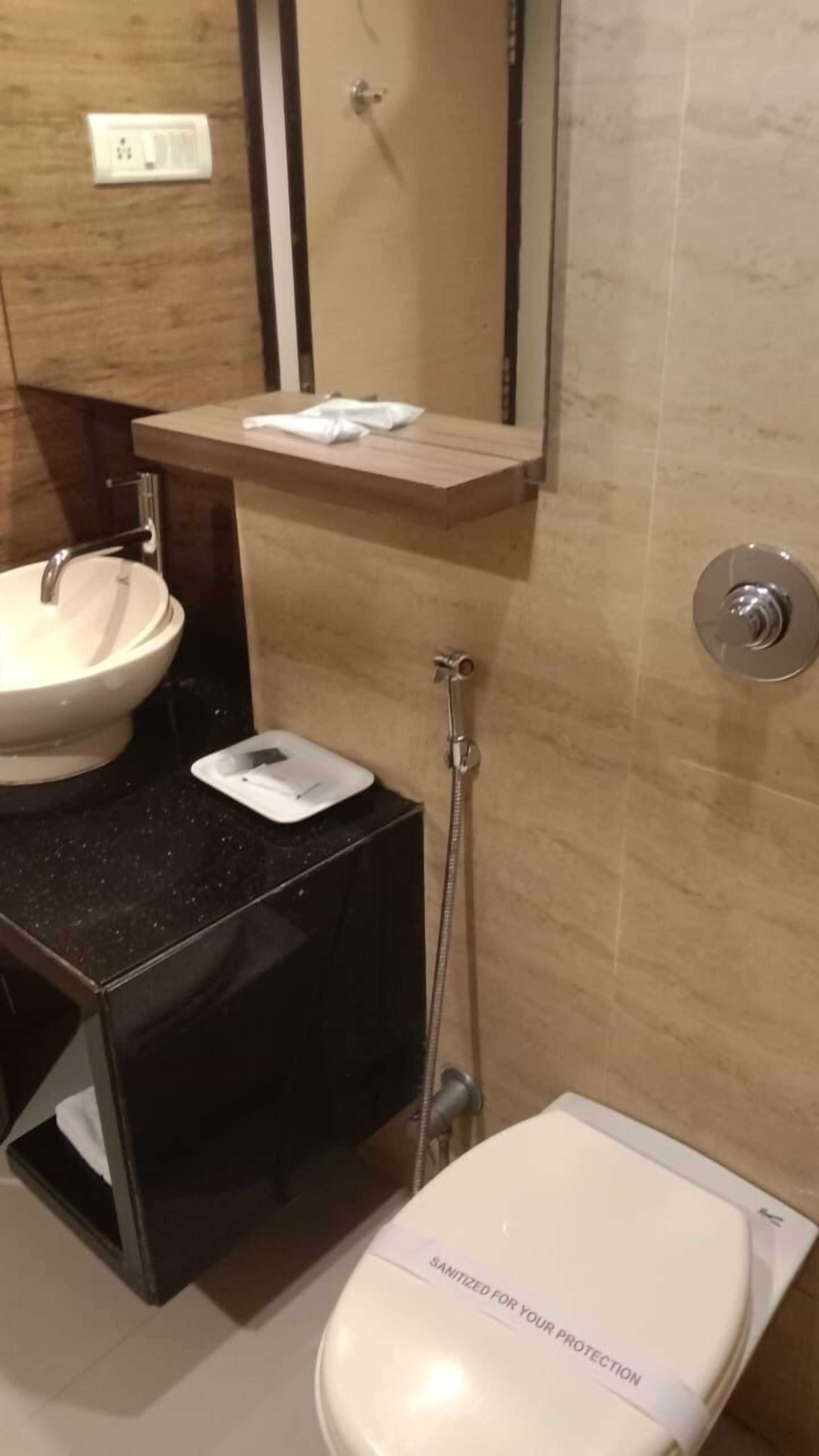 Une salle de bain moderne avec un lavabo blanc, un plan de toilette noir, un miroir au-dessus du lavabo et une pomme de douche.