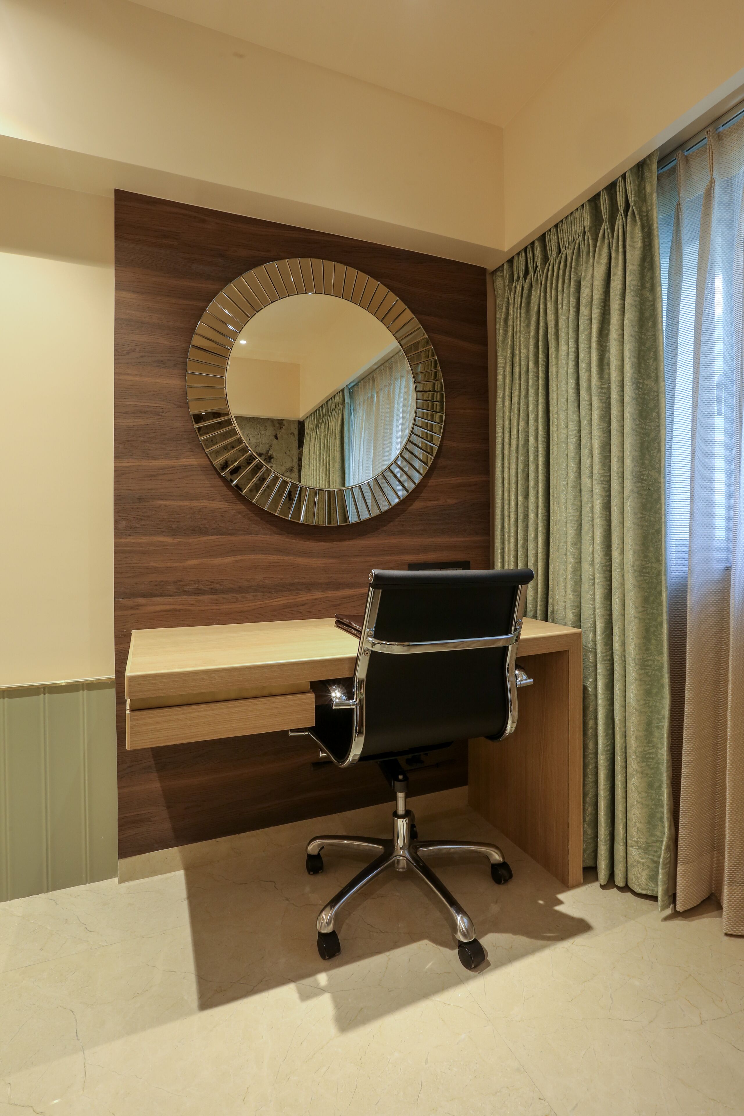 Un espace de bureau moderne avec un bureau en bois, une chaise de bureau noire et un grand miroir au mur.