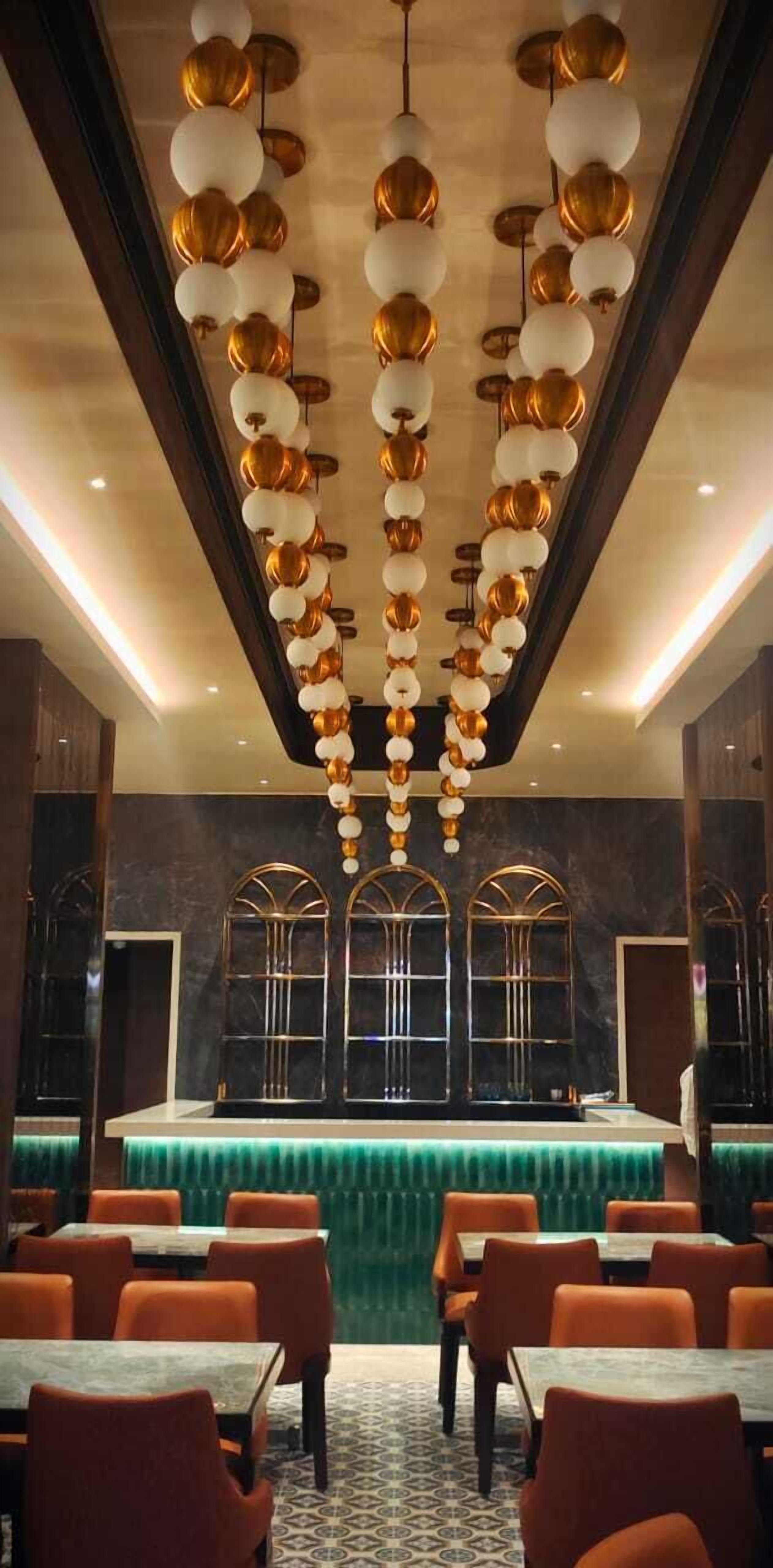A restaurant with a long table, orange chairs, and a ceiling with hanging spherical light fixtures.