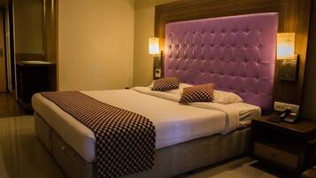 A hotel room with a large bed, a wooden headboard, two bedside lamps, and a nightstand with a phone.