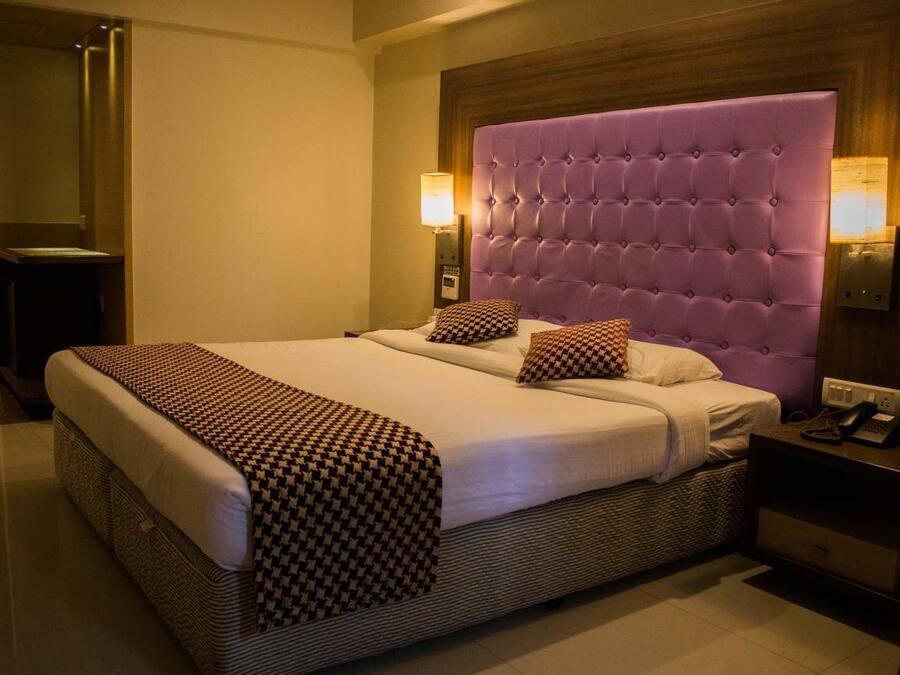 A hotel room with a large bed, a wooden headboard, two bedside lamps, and a nightstand with a phone.