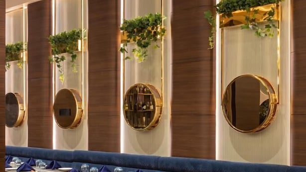 A restaurant with a long counter, orange chairs, and round mirrors on the wall.