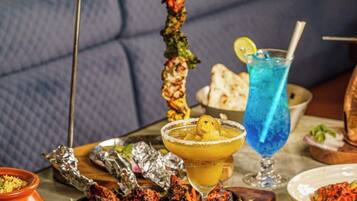 A dining table with various dishes, including grilled meat, a tall skewer, and a blue drink.