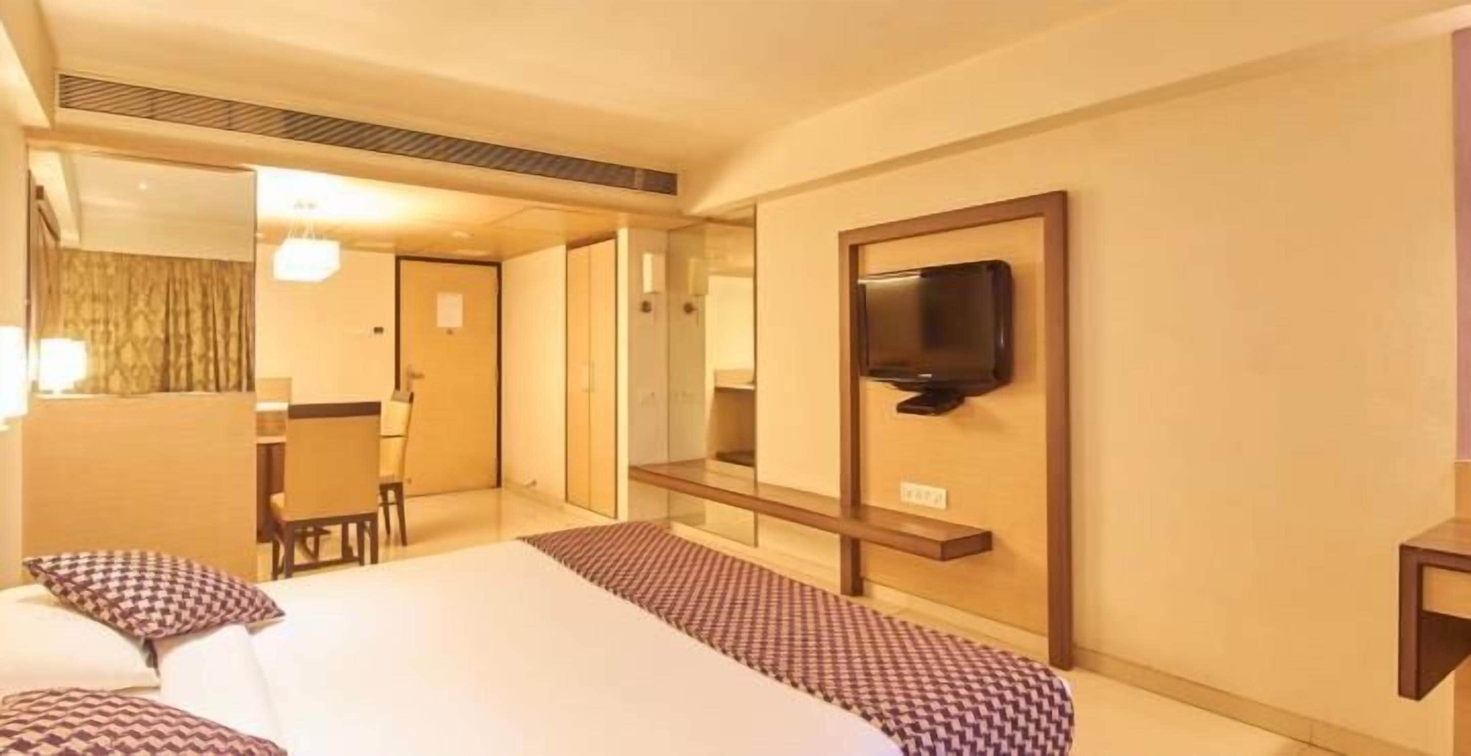 A hotel room with a bed, a television mounted on the wall, a small table, and a chair.