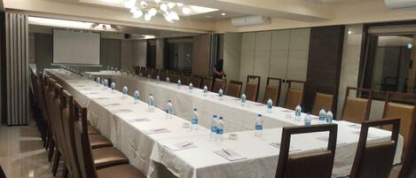Un salón de conferencias con una larga mesa, sillas, botellas de agua y una pantalla para proyector.