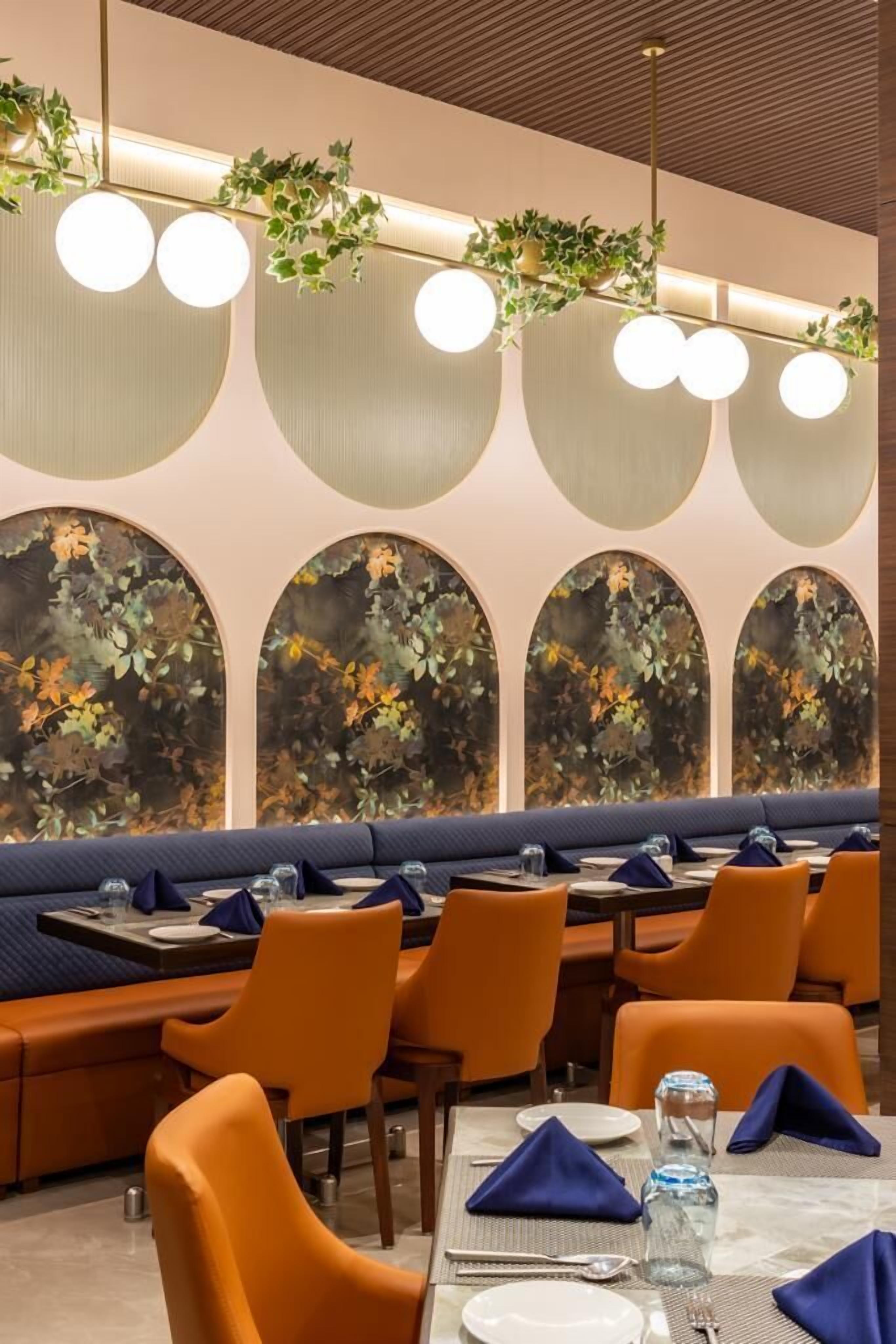 Un intérieur de restaurant moderne avec des tables rondes, des chaises orange et un banc bleu rembourré.