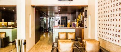 A modern hotel lobby with leather seating, a reception desk, and a wall with a leaf pattern.