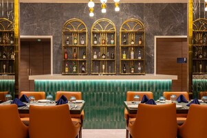 A bar area with three shelves of liquor bottles, orange seating, and a green bar counter.