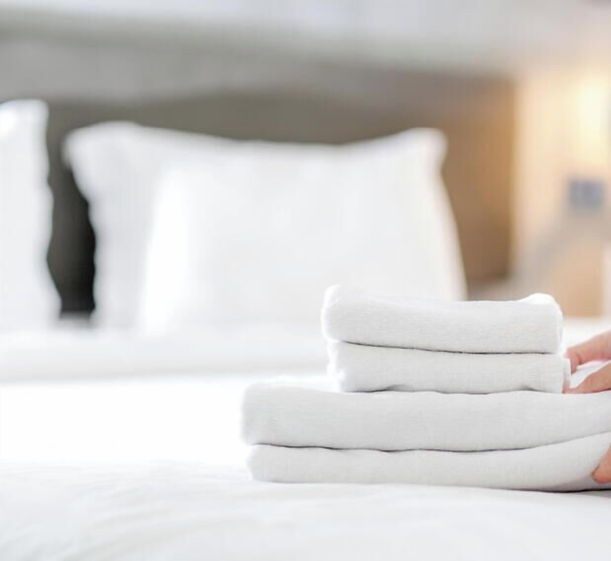 A person folding a stack of white towels on a bed.
