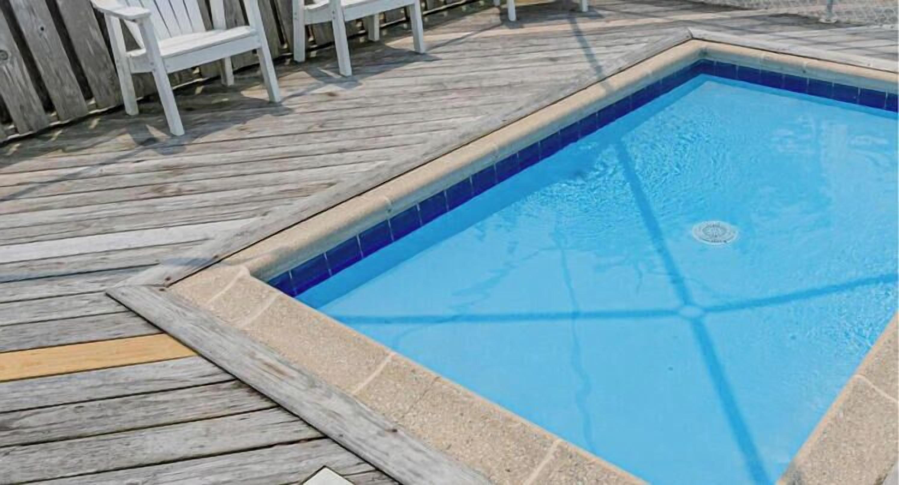 A rectangular swimming pool with a tiled edge, surrounded by a wooden deck.