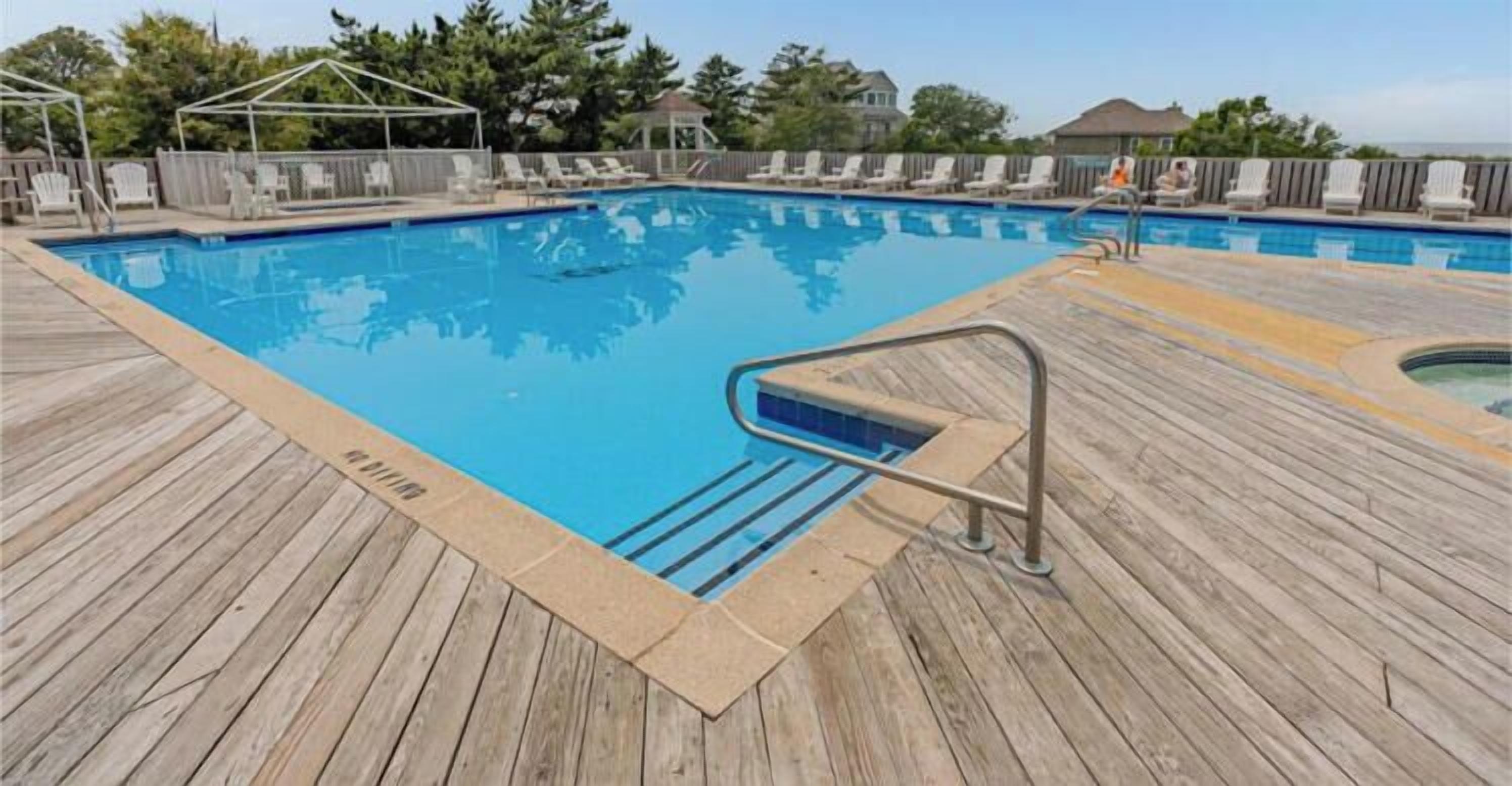 A wooden deck surrounding a rectangular swimming pool with a metal ladder.
