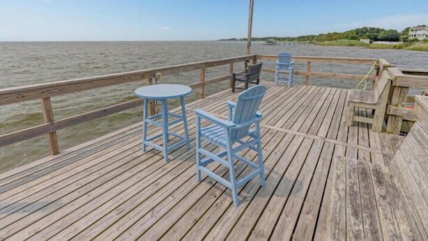 Une terrasse en bois avec une table et des chaises, donnant sur une étendue d’eau.