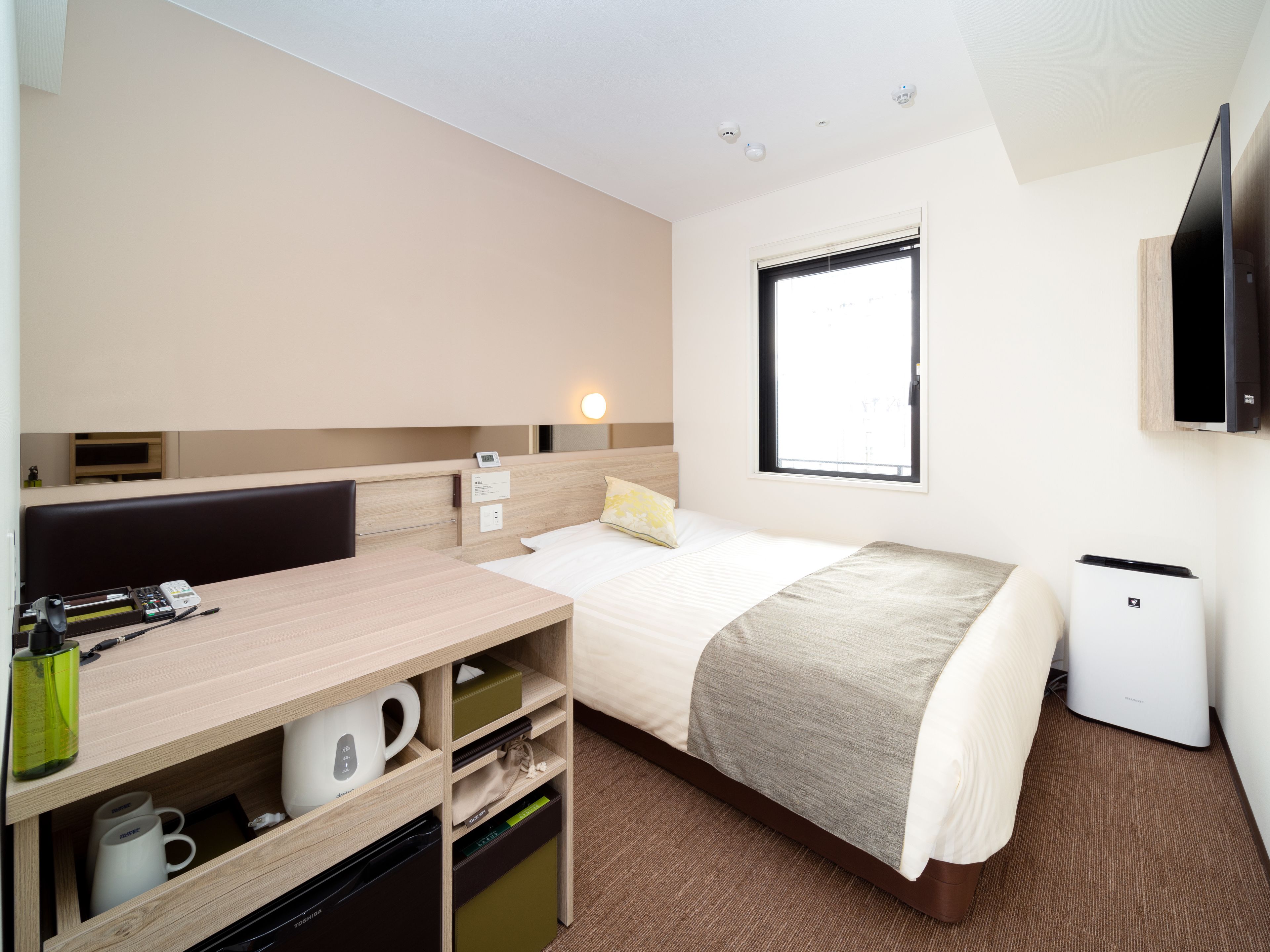 Une chambre d’hôtel comprenant un lit, un bureau avec une chaise, une petite table, un téléviseur et une fenêtre.
