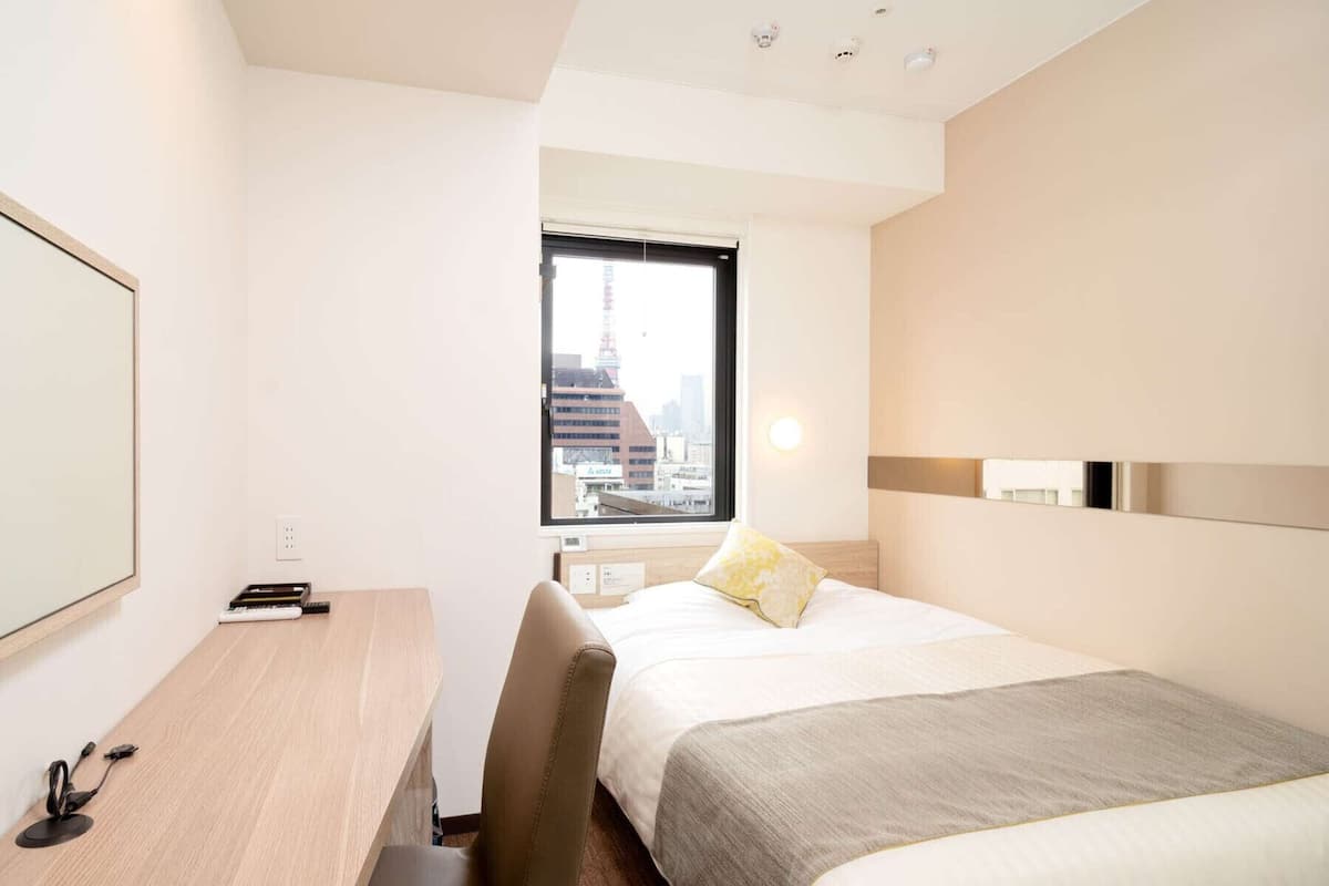 A hotel room with a desk, chair, bed, and a window with a city view.