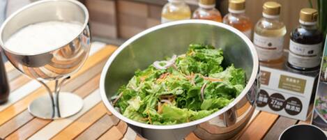 A salad bowl on a wooden table with a glass of milk and bottles of condiments in the background.