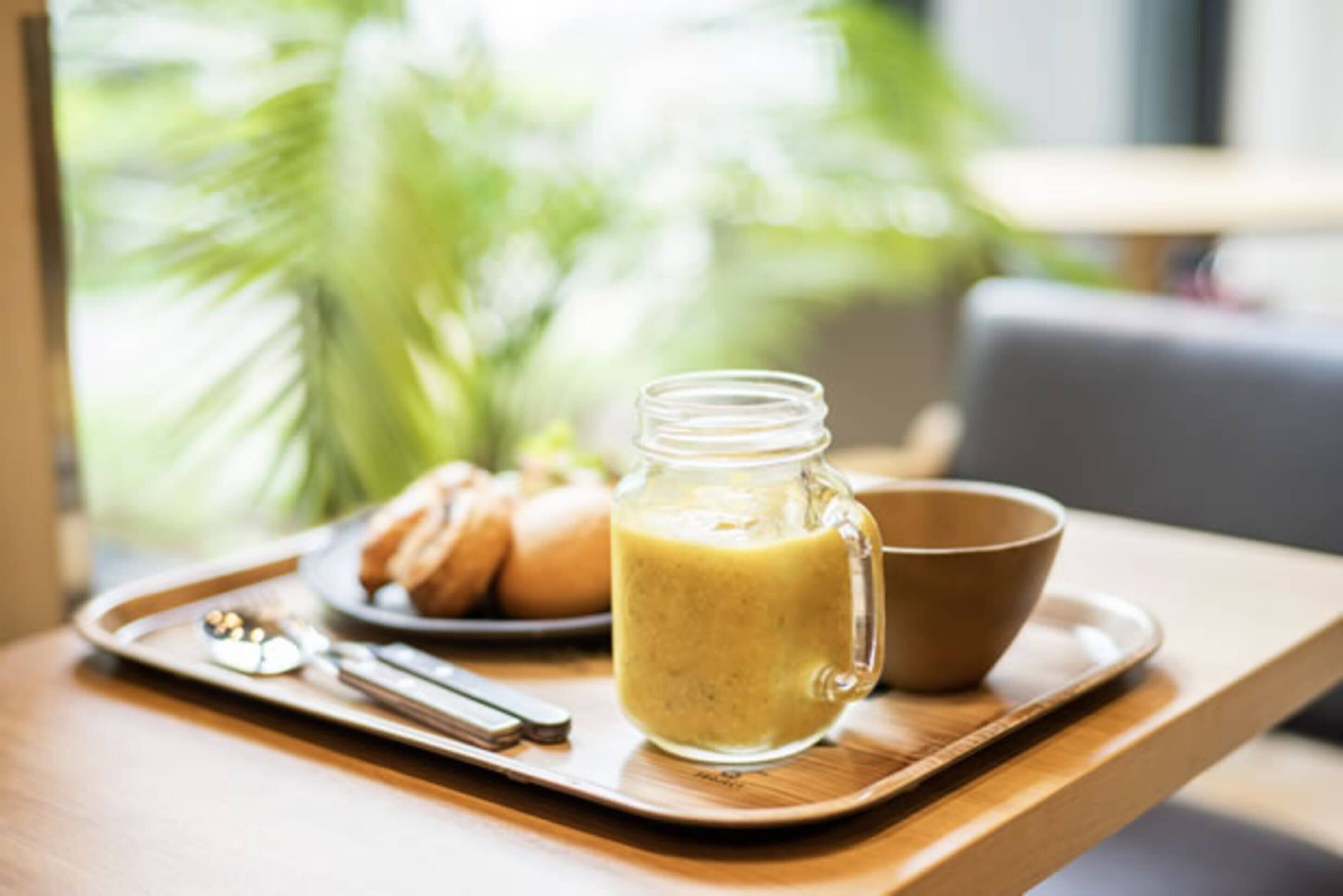 Aamiaistarjotin, jossa on lasipurkki täynnä smoothiea, kulho ja croissant-leivoksia puupöydällä.
