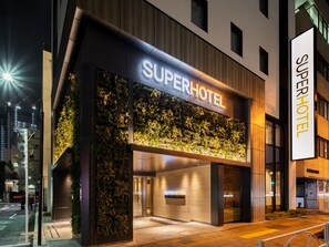 Moderni hotelli, jossa on selkeästi näkyvä «SuperHotel»-kyltti, pystysuora viherseinä ja tyylikäs, nykyaikainen muotoilu.