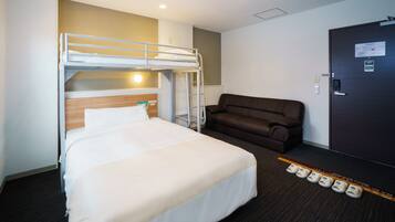 Une chambre d’hôtel avec un lit superposé, un canapé, une porte avec une serrure et un porte-chaussures contenant des chaussures.