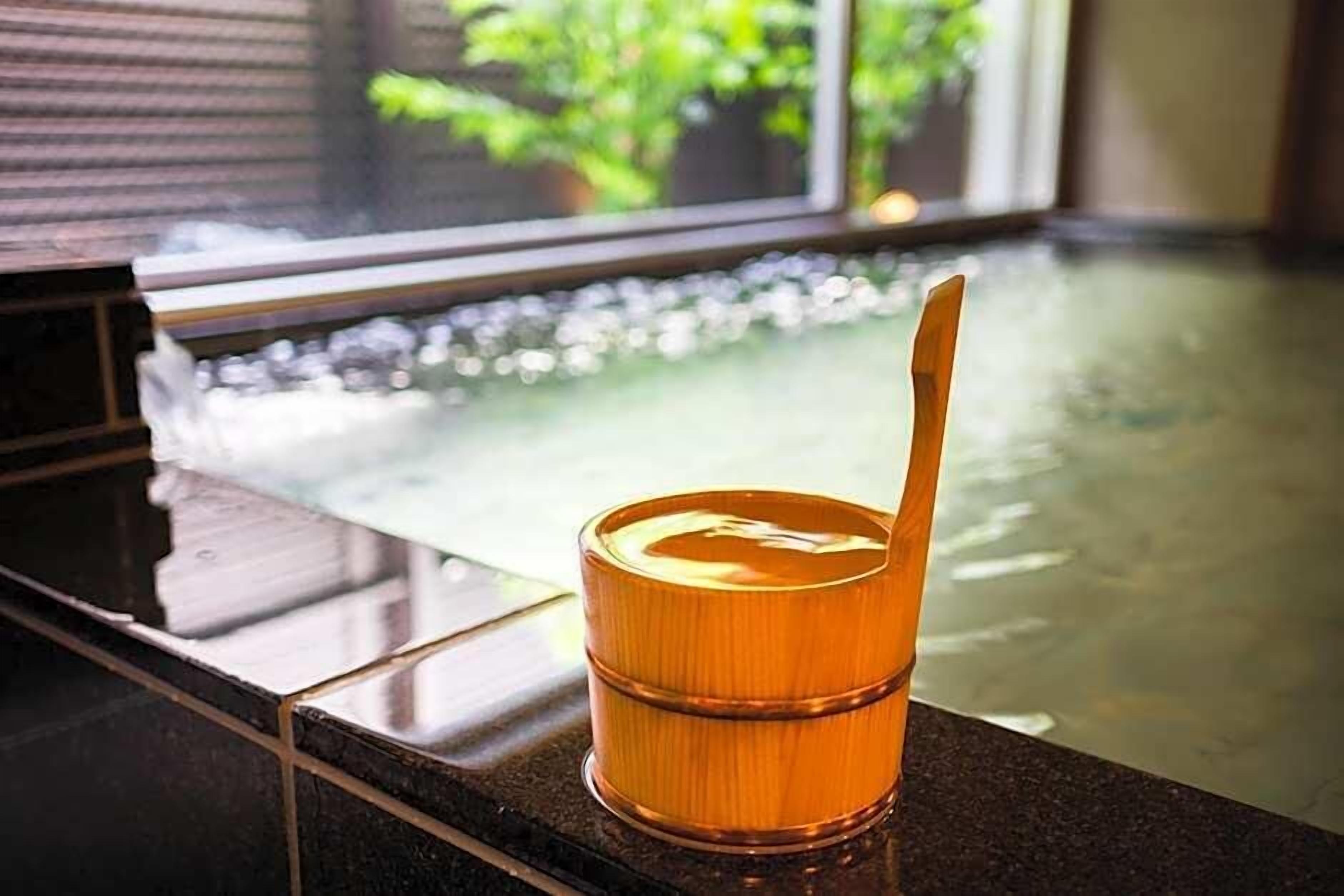 A glass of amber liquid with a straw on a reflective surface near a window with a view of greenery.