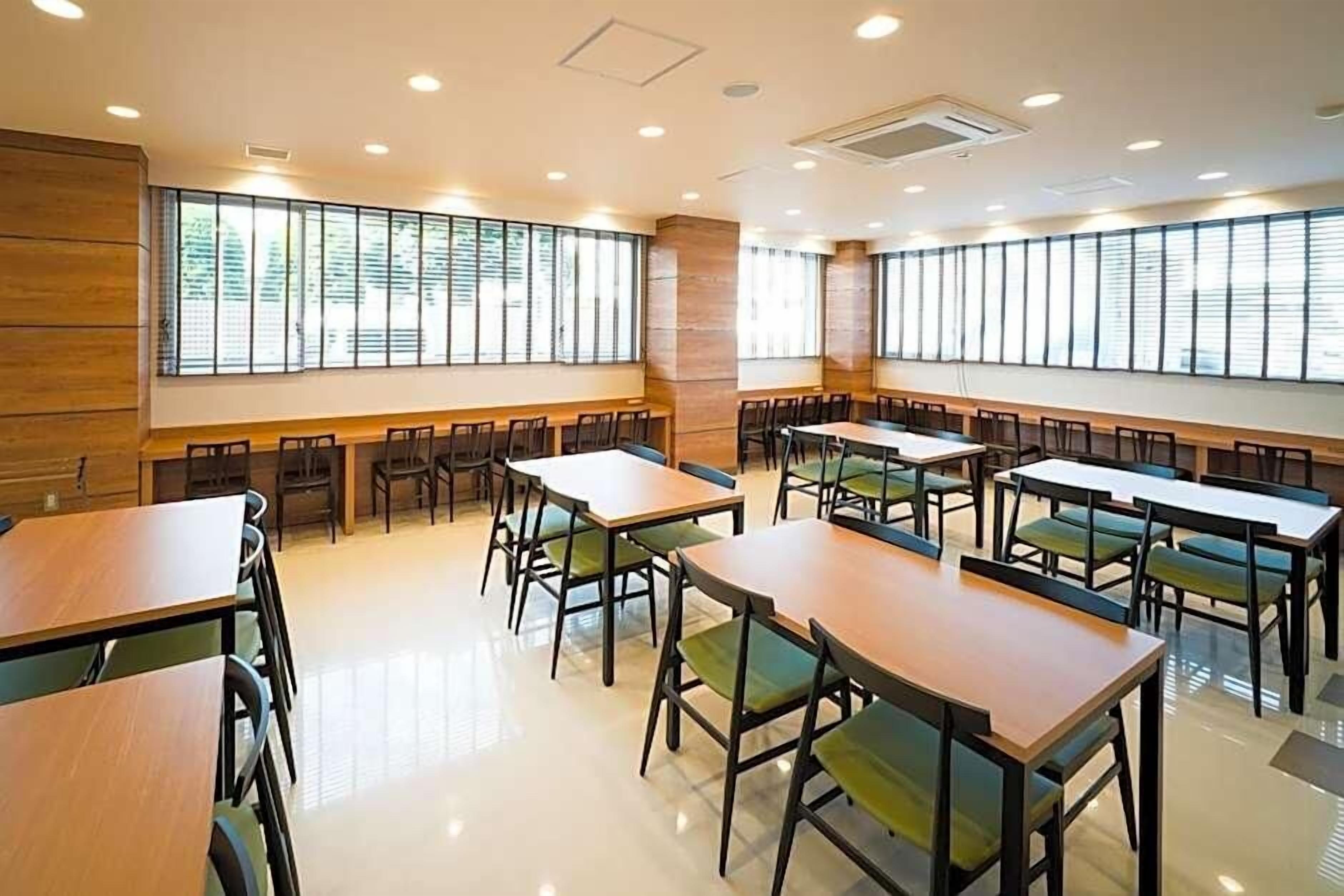 A conference room with multiple tables and chairs, large windows, and a polished floor.