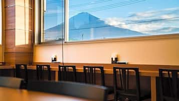 A dining area with a long table and chairs, large windows with a view of a mountain, and a wooden wall.