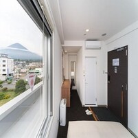 A hotel room with a bed, a window with a view of a mountain, a hallway, and a door.