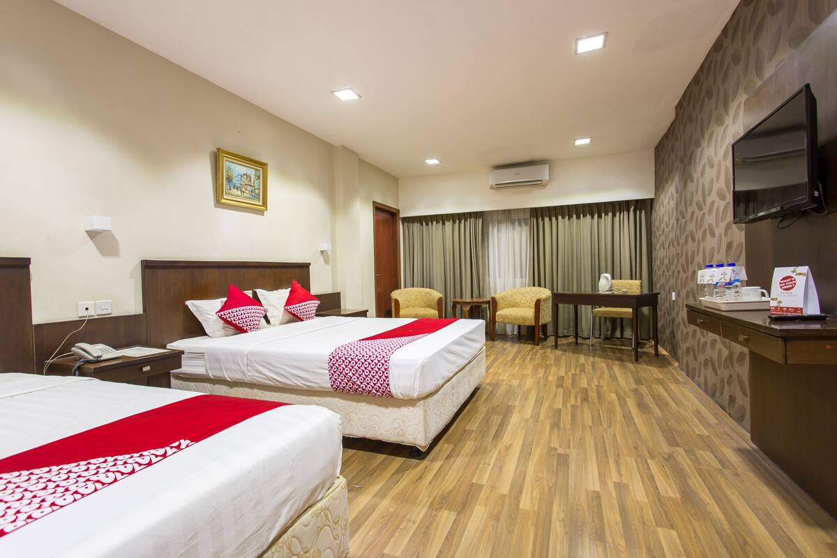 A hotel room with two beds, a desk, a chair, a television, and an air conditioning unit.