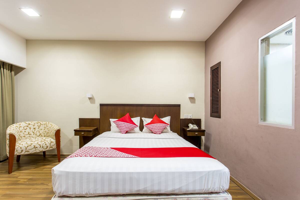 A hotel room with a bed, a chair, a nightstand, and a window.