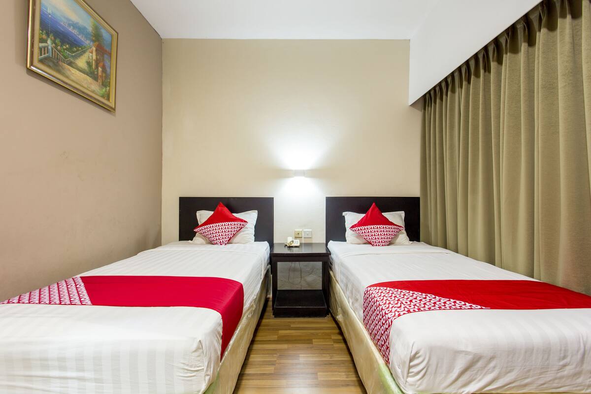 A hotel room with two beds, each with red and white bedding, a nightstand between them, and a painting on the wall.