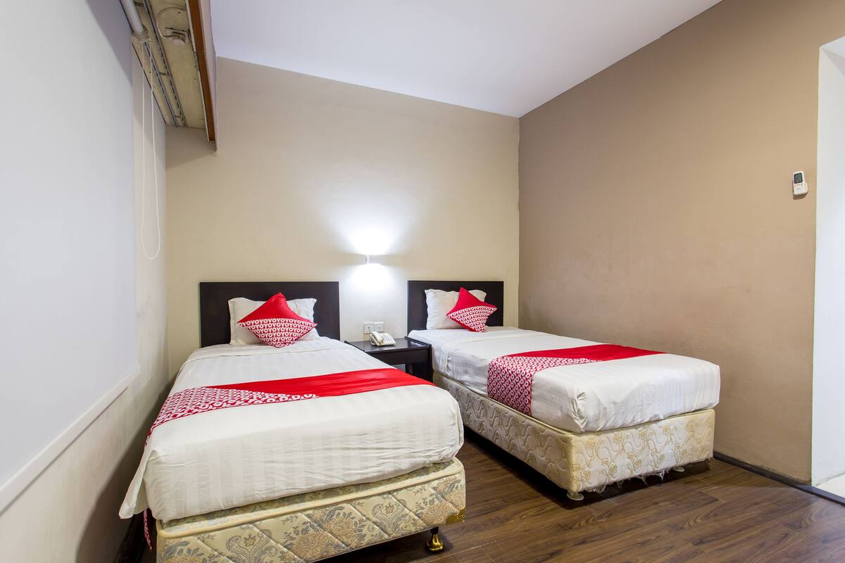 A hotel room with two beds, each with a red and white bedspread, and a nightstand between them.