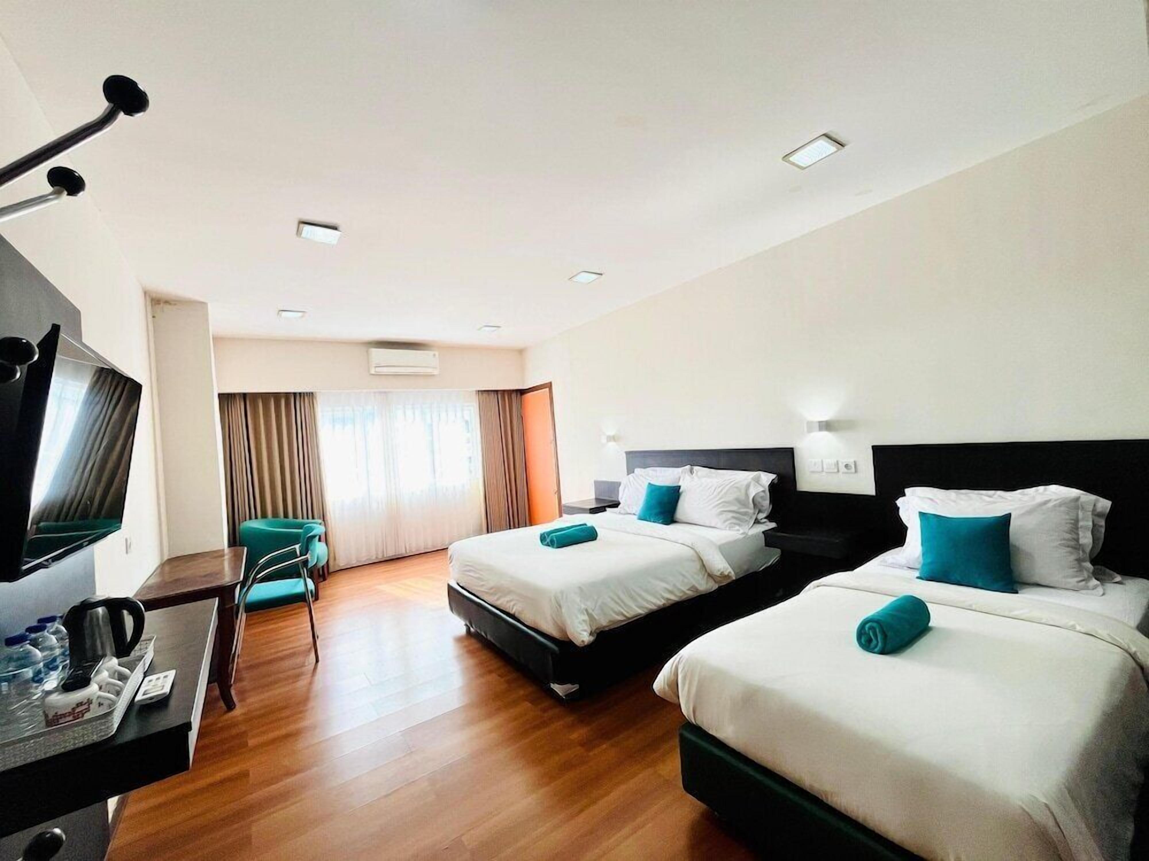 A hotel room with two beds, a TV, a desk with a coffee maker, and a view of the outdoors.