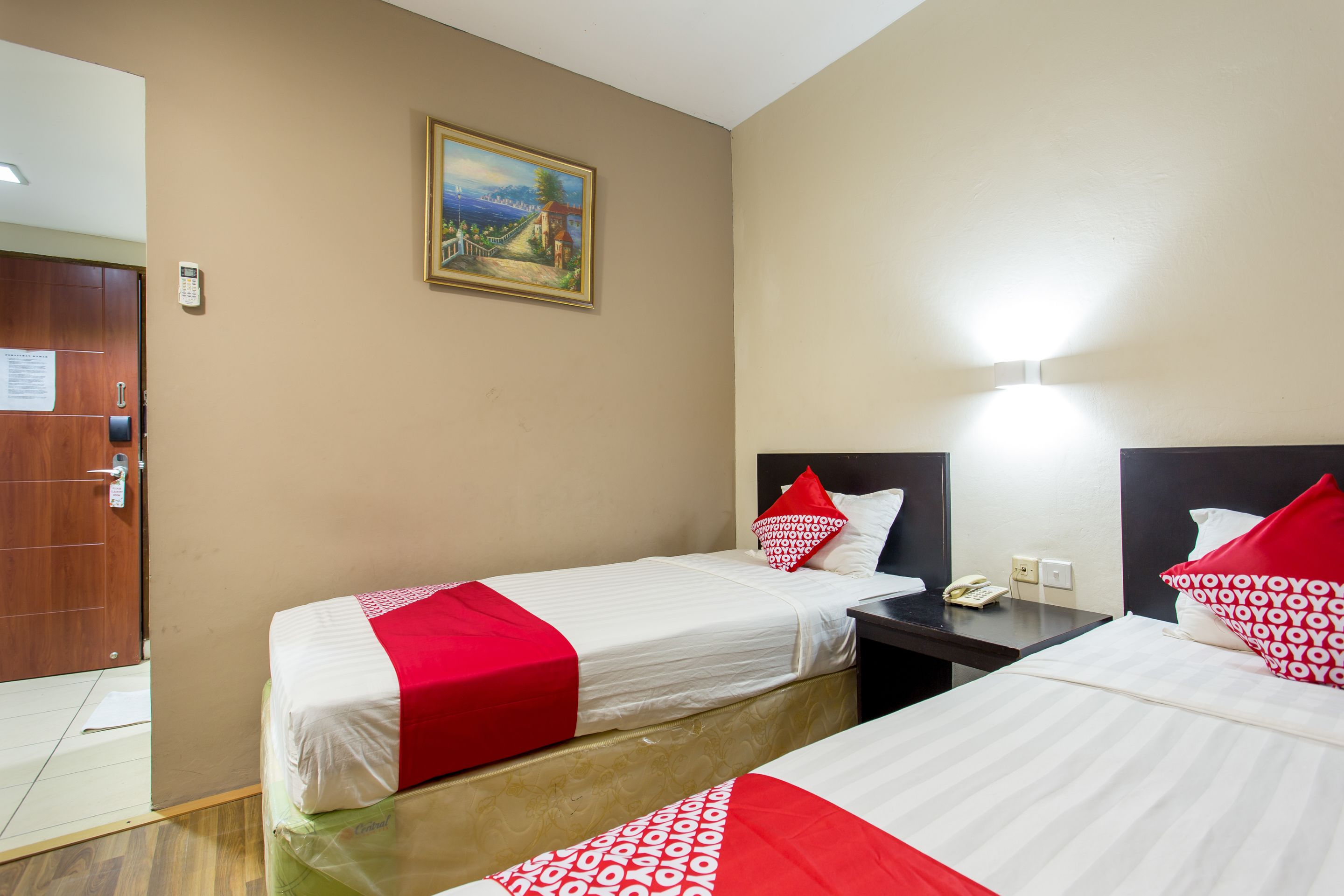 Habitación de hotel con dos camas, un cuadro en la pared y una puerta con un cartel.