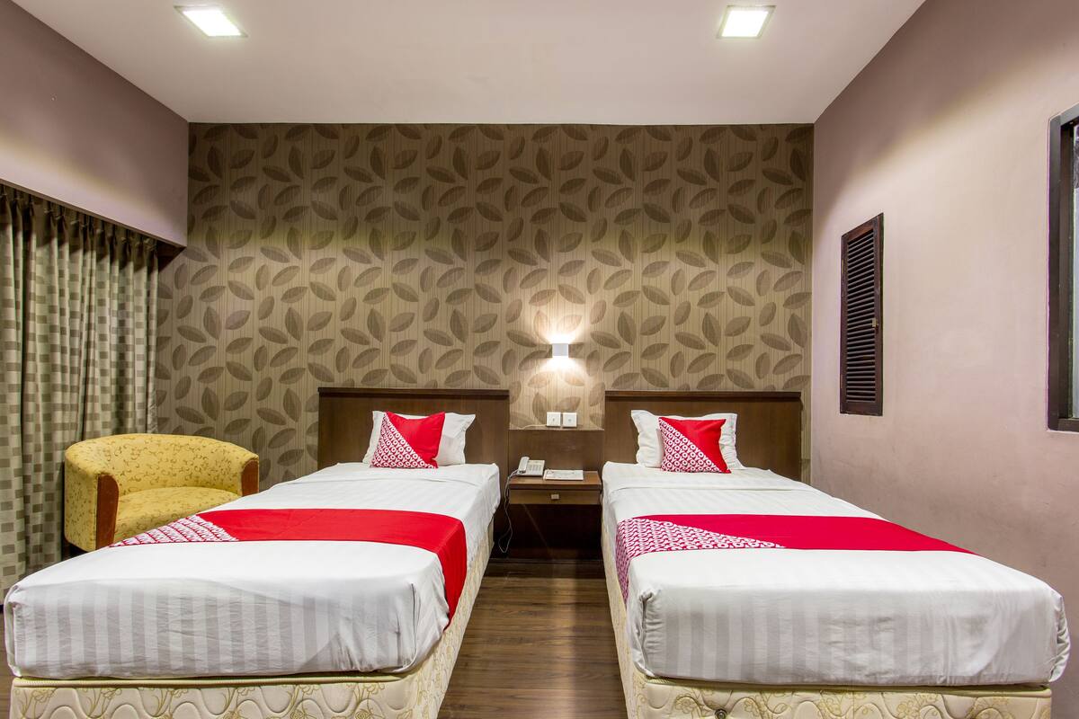 A hotel room with two beds, a nightstand, a lamp, a chair, and a patterned wallpaper.