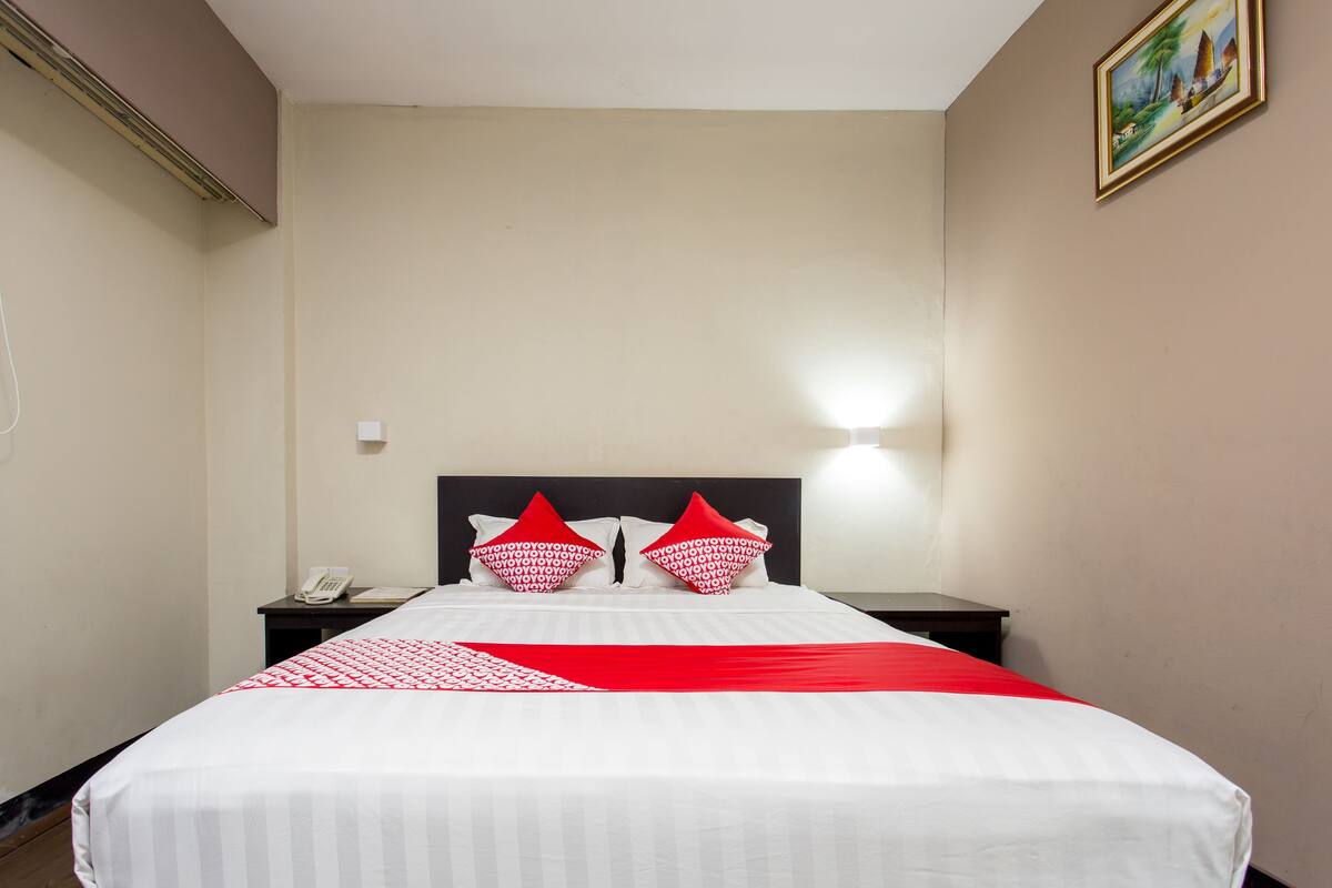 A hotel room with a bed, two nightstands, a telephone, and a wall-mounted light.