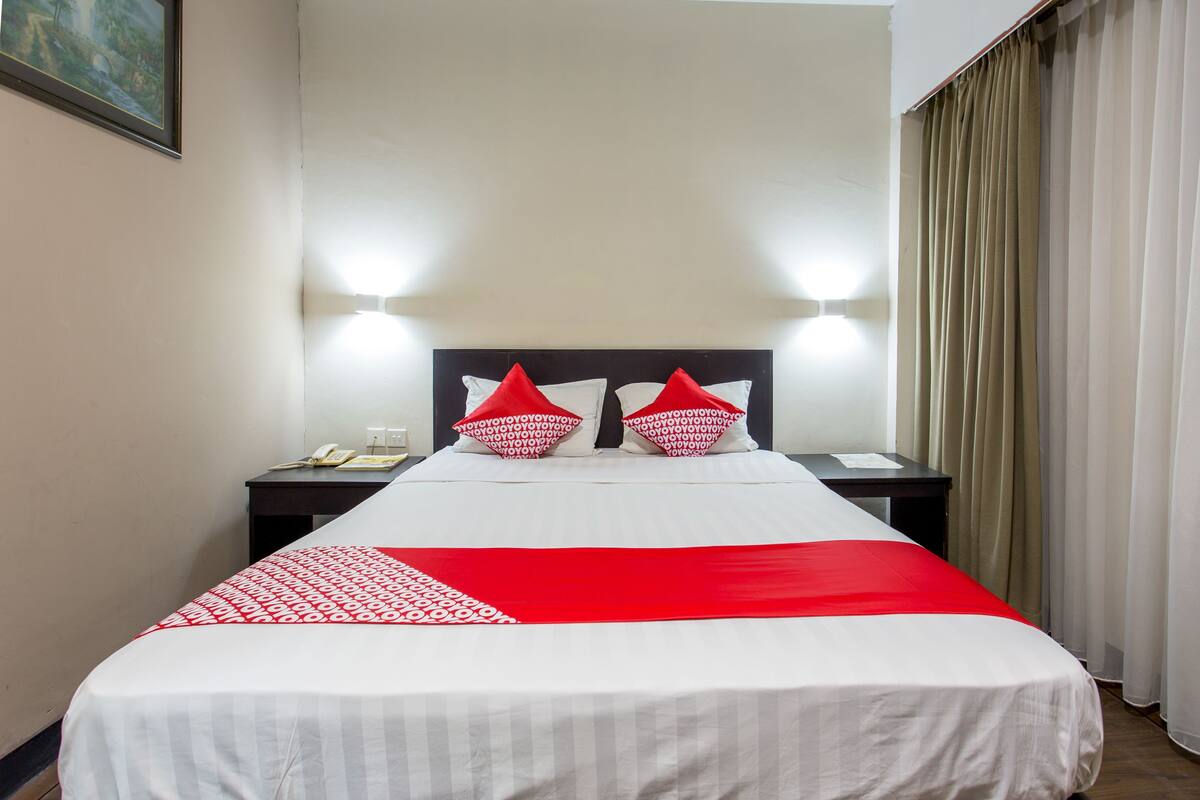 A hotel room with a large bed, two bedside tables, a nightstand, and a wall-mounted light fixture.