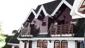 A traditional house with a steeply pitched roof, multiple windows, and a balcony. - Casa em Campos do Jordão (Campos do Jordão)