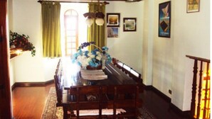 A dining room with a wooden table, chairs, and a floral centerpiece. There are framed pictures on the walls and a staircase to the right. - Casa em Campos do Jordão (Campos do Jordão)