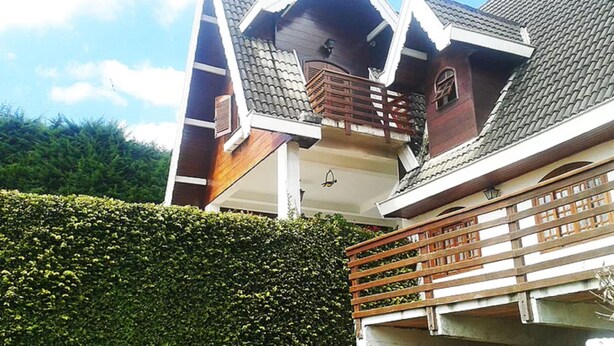 A multi-story house with a balcony, a wooden fence, and a well-maintained hedge. - Casa em Campos do Jordão (Campos do Jordão)