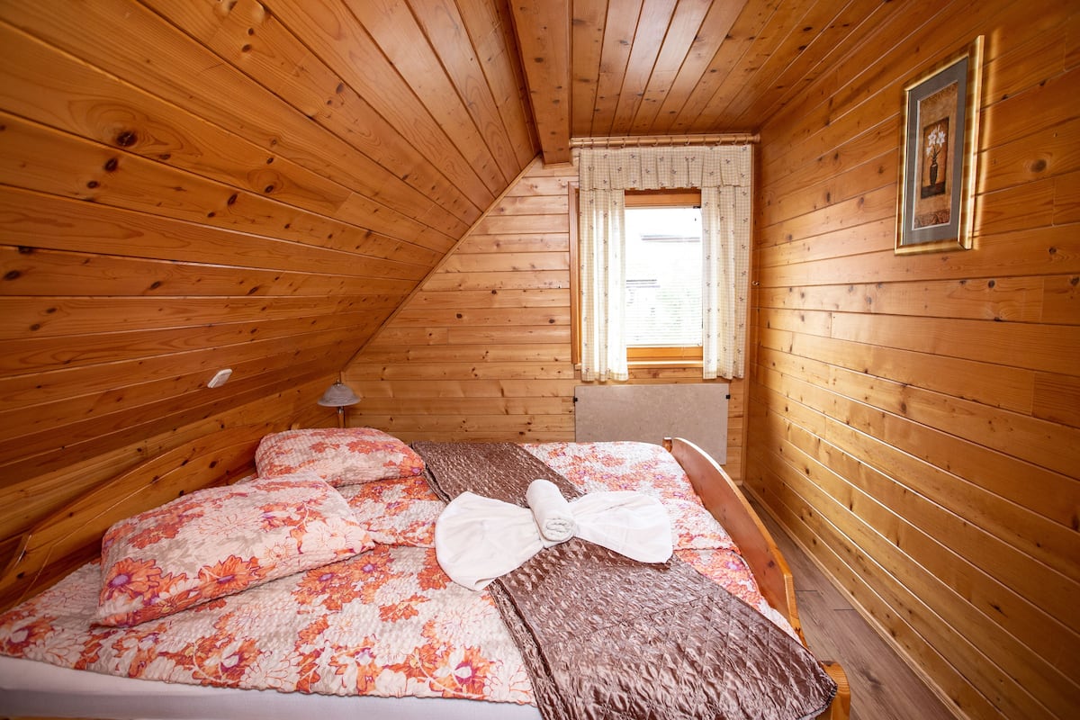 Une pièce aux murs lambrés, avec un lit, une fenêtre avec des rideaux et un tableau encadré accroché au mur.