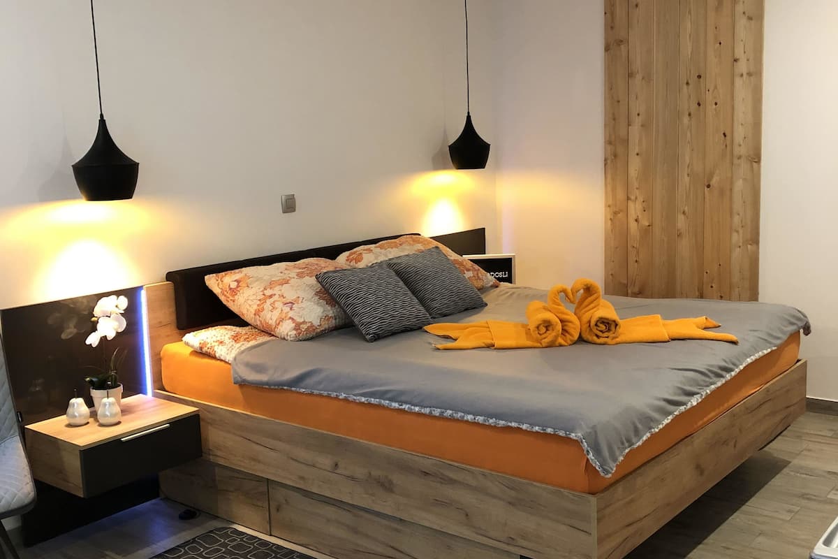 Une chambre à coucher moderne avec un lit en bois, deux tables de chevet, une commode, un tapis noir et des lampes suspendues.