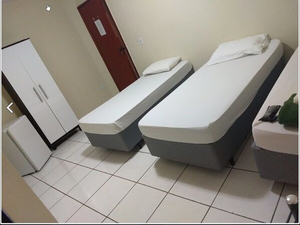 A room with two single beds, a white wardrobe, and a small refrigerator.