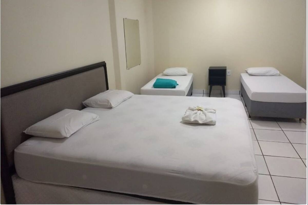 A hotel room with a large bed, two smaller beds, a nightstand, and a mirror on the wall.