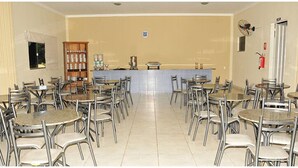 A dining area with multiple tables and chairs, a counter with a cash register, and a fire extinguisher on the wall. - Hotel Boa Viagem (Barra do Garcas)