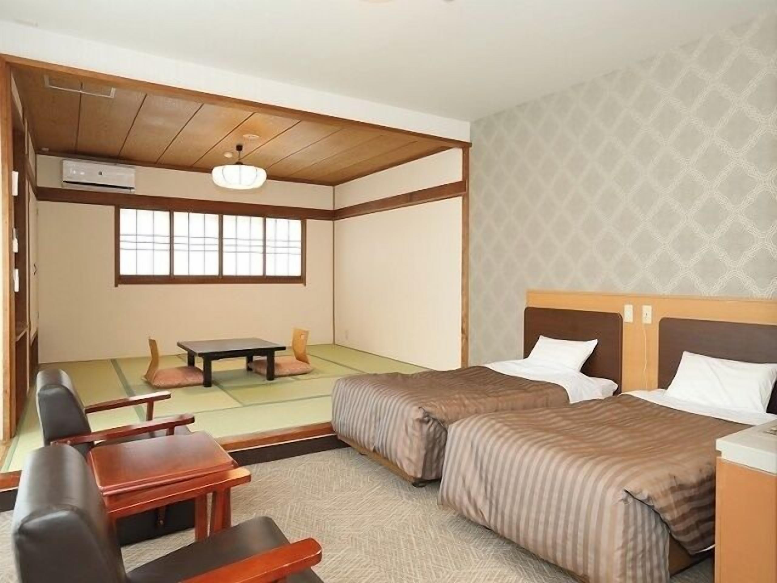Una habitación tradicional japonesa con suelo de tatami, techo de madera bajo, futón, una mesita y una silla.