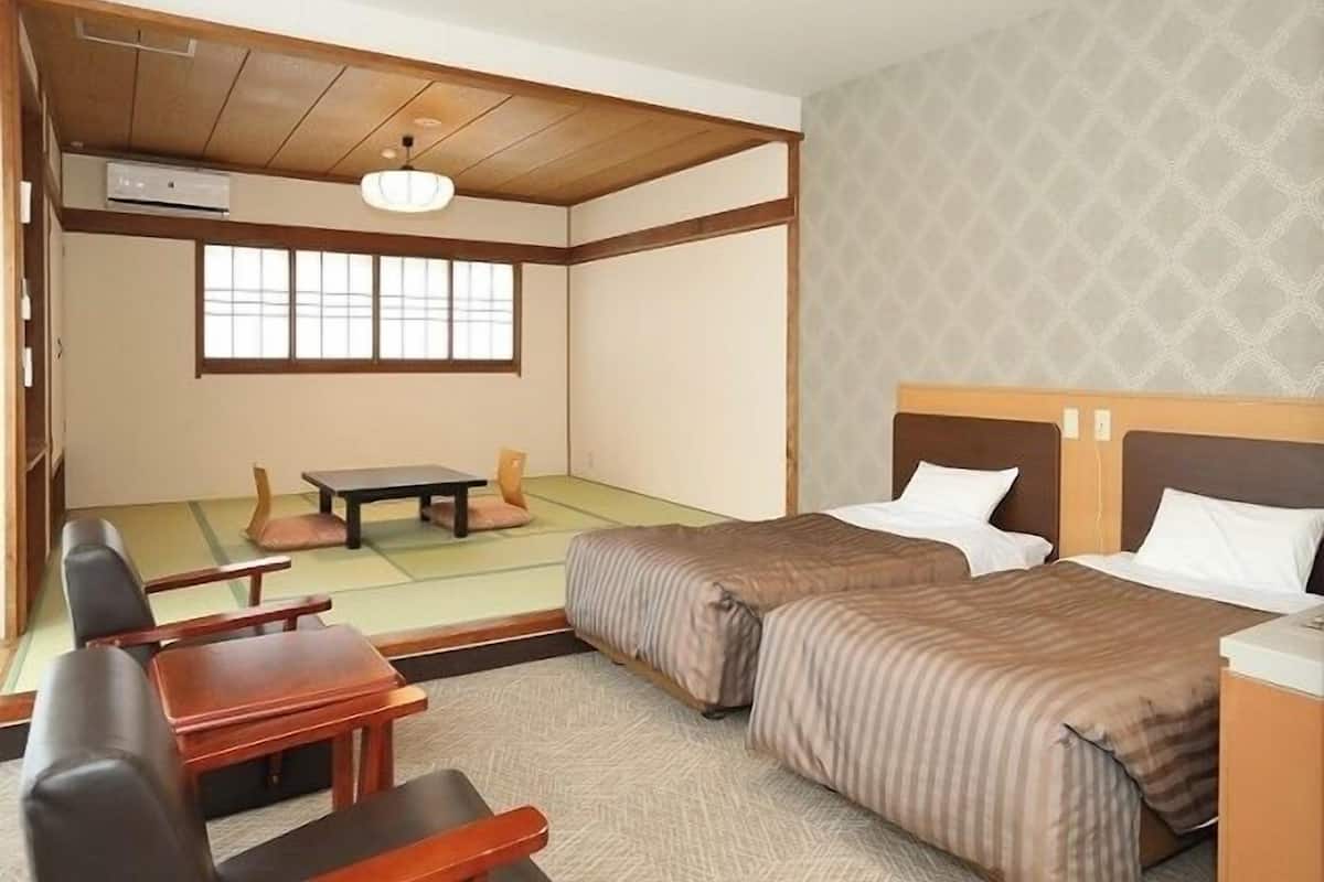 Una habitación tradicional japonesa con suelo de tatami, techo de madera bajo, futón, una mesita y una silla.